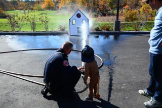 Fire fighter outside with child spraying hose
